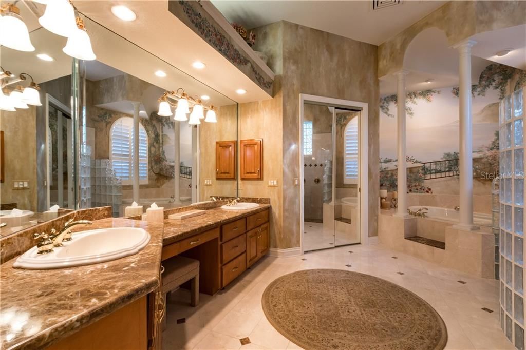 bathroom with lanscape painting behind soaking tub, wall of mirrors, and circular rug