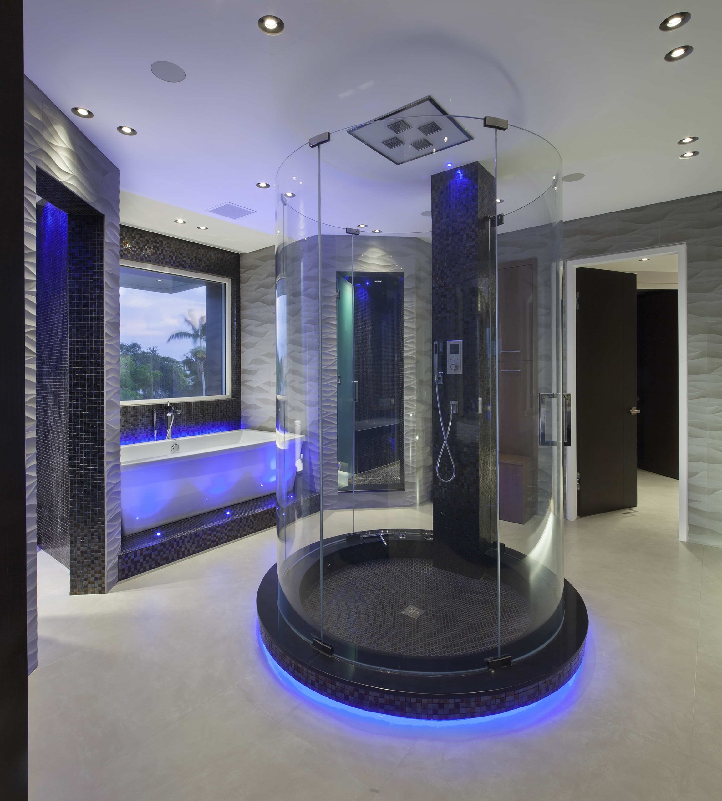 unique bathroom with circular glass shower in middle of room, glowing blue, with a soaking tub 