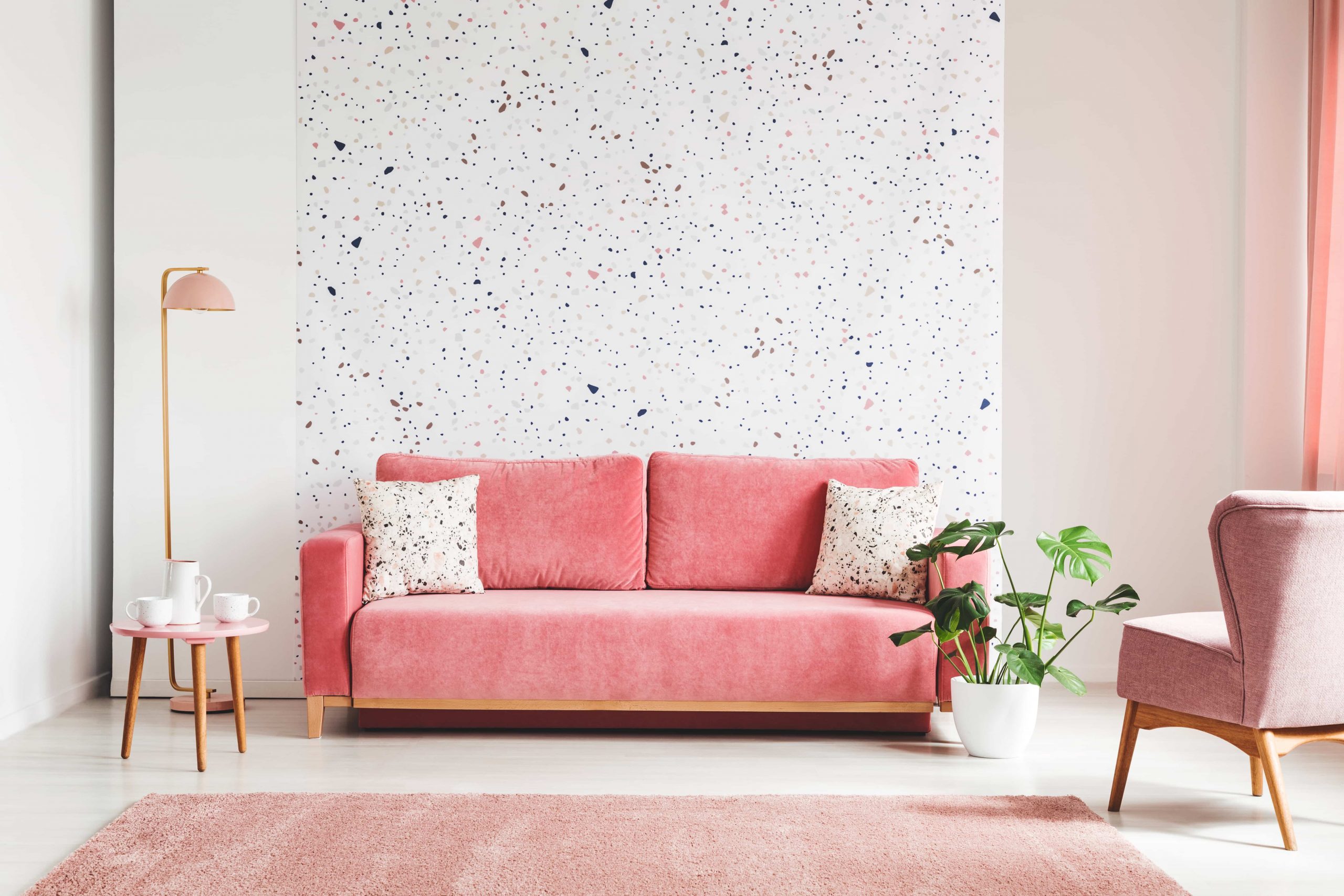 pink, velvet sofa, plant, coffee table with pot and cups on a lastrico wall a living room interior