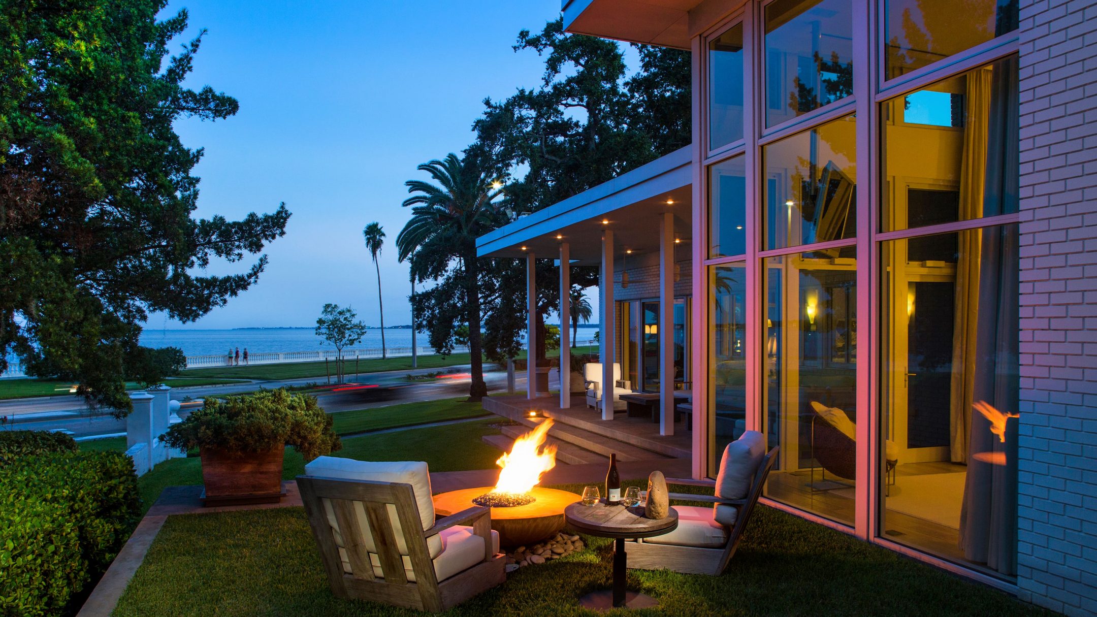 Picture of a luxury house with water view, an outdoor fireplace, and many windows.